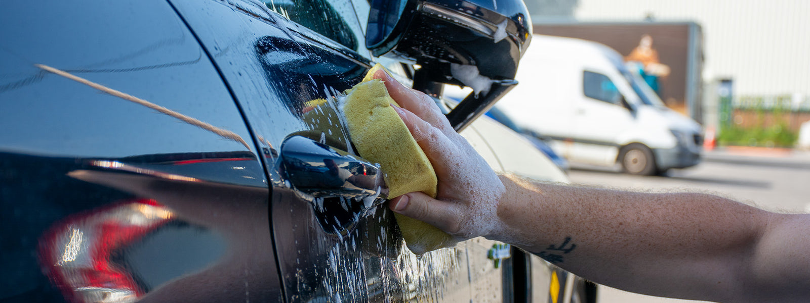 Sponge being used to wash a car in a driveway