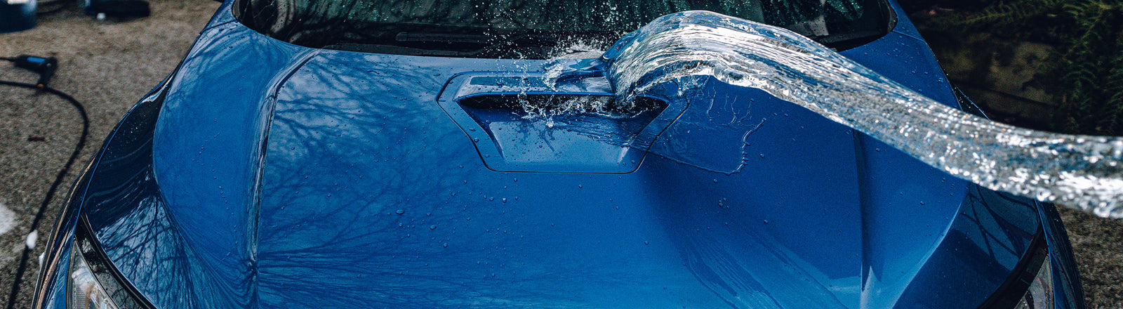Two detailing buckets beside a car on a driveway with an unused hosepipe coiled nearby