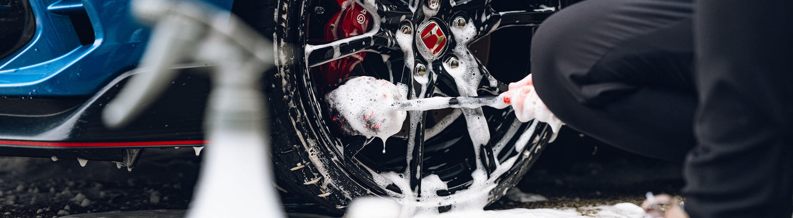 Rinsing a car bonnet with a watering can beside two detailing buckets