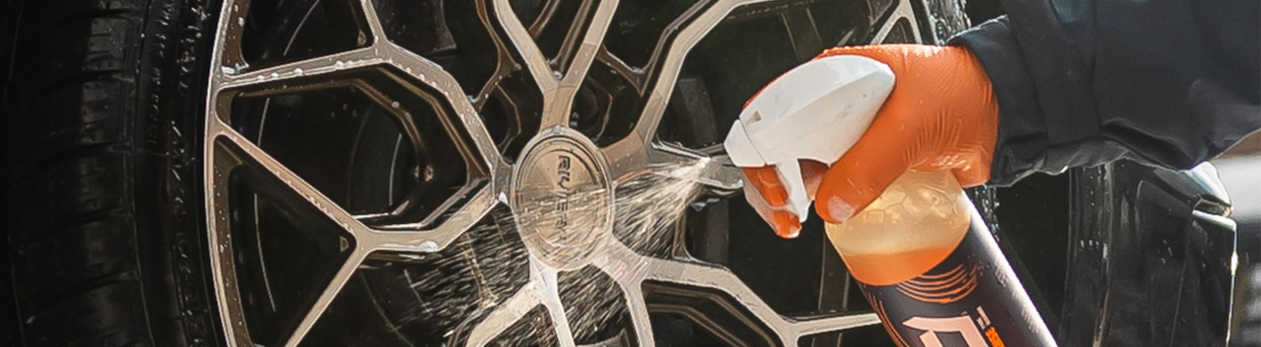 Green nitrile glove gripping a wet alloy wheel during car detailing